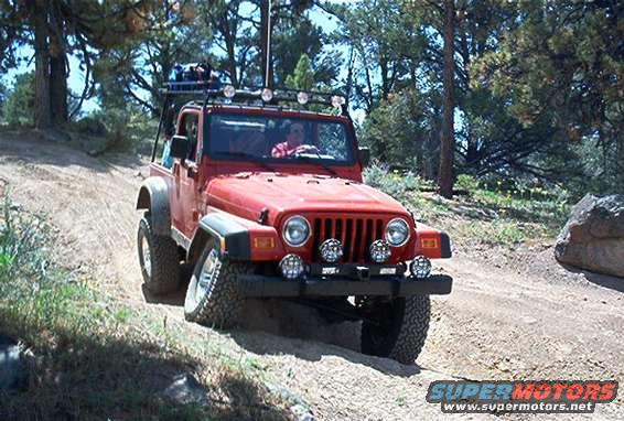 Red Jeep Wrangler driving on a dirt road with trees and rocks around