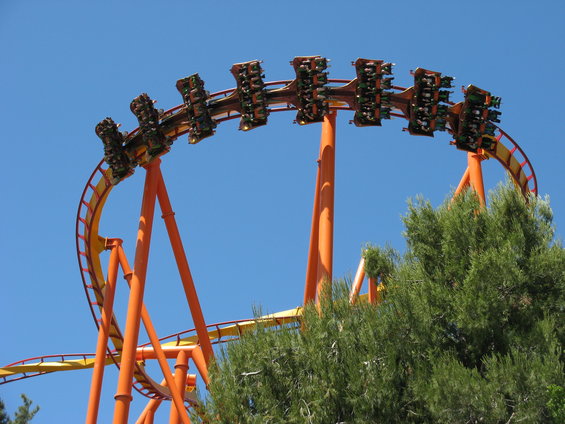 Orange roller coaster track with cars full of riders against a blue sky