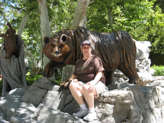 Woman sits on rocks in front of a large bear statue. Another smaller bear statue is visible to the left