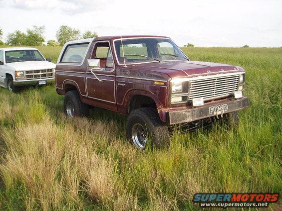 Maroon 1980 Ford Bronco with white top and trim, 3q-front view in tall grass