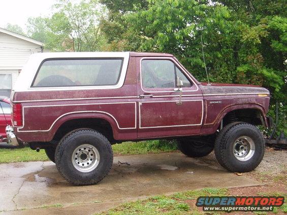 Maroon Ford Bronco with a white top, lifted with large tires. Side view