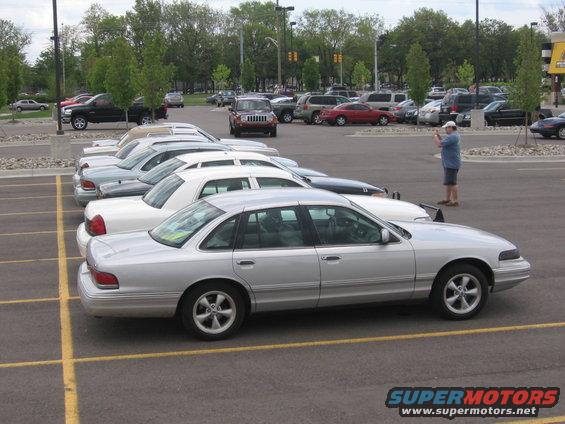 Silver sedan parked in a lot, a guy stands taking a photo