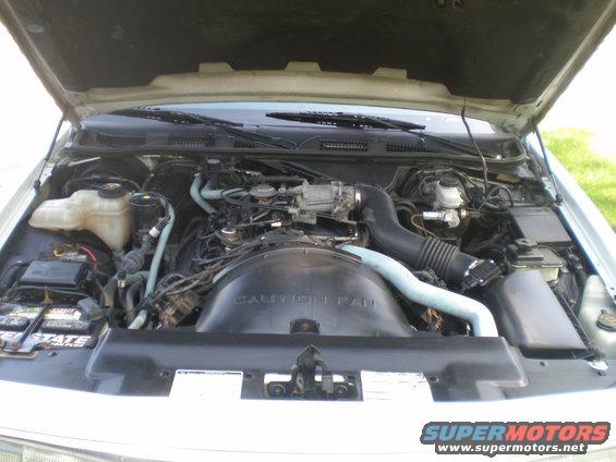 Engine bay with "CAUTION FAN" shroud and blue hoses