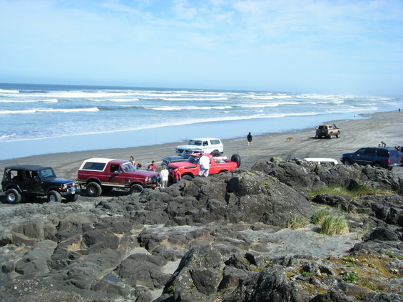Several off-road vehicles parked on a rocky beach near the ocean