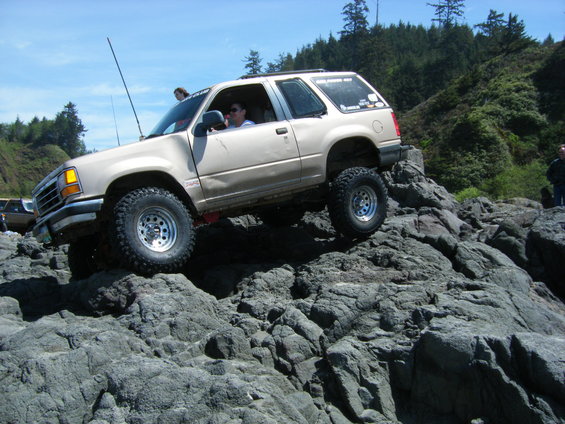 Tan SUV with lifted suspension and off-road tires navigating a rocky terrain