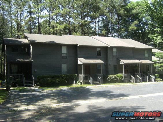 Townhouses with trees behind them. A "SUPERMOTORS" watermark is in the bottom right