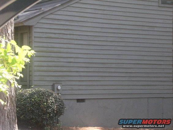 Side view of a gray building with horizontal siding and a green bush