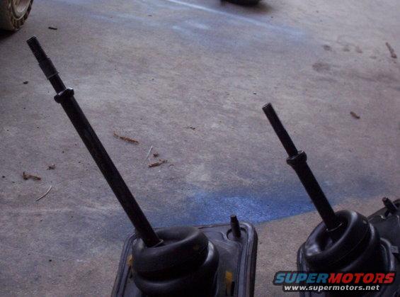 Two car gear shift levers with rubber boots on a concrete floor