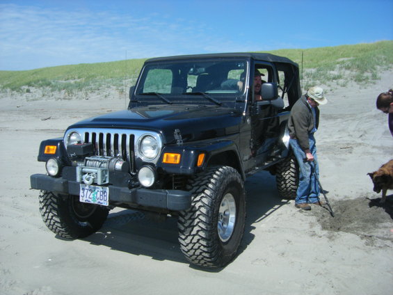 Black Jeep Wrangler with winch and off-road tires on a sandy beach