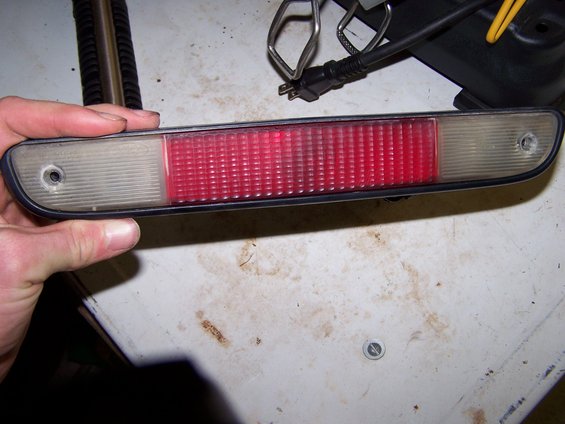Hand holding a red and clear plastic third brake light assembly with a black rubber gasket