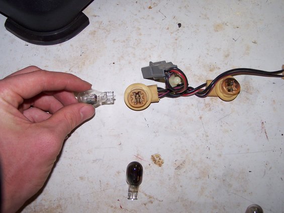 Hand holding a clear light bulb next to a tan socket with wires