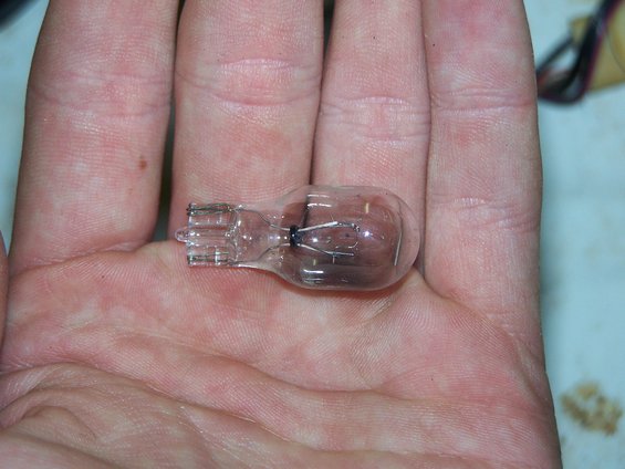Automotive wedge base incandescent light bulb held in a palm