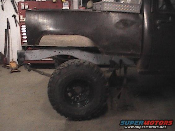 Truck bed and chassis with large tire, jack stands, and tools in background