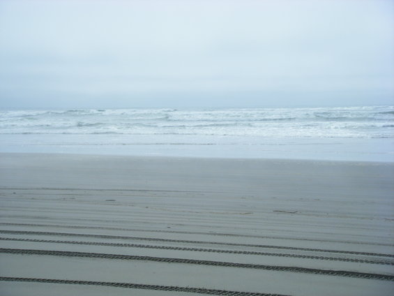 Tire tracks on a sandy beach with ocean waves in the background