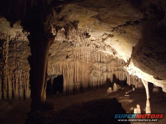 Cave interior with stalactites and stalagmites, Supermotors.net logo in corner