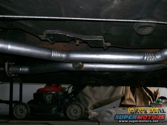 Underside view of dual exhaust pipes and undercarriage of a vehicle, with a lawnmower visible below