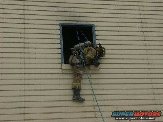 Firefighter in full gear rappelling down the side of a building through a window