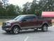 2005 Ford F-150 - Maroon and tan Ford F-150 truck parked on asphalt with trees and a fence in the background.