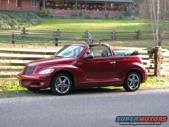 Red convertible Chrysler PT Cruiser parked on a road next to a wooden fence