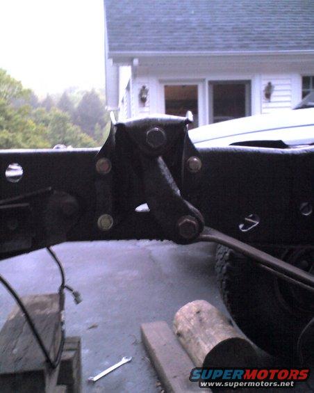 Close-up of a black metal bracket bolted to a truck frame, with a wrench on the ground nearby