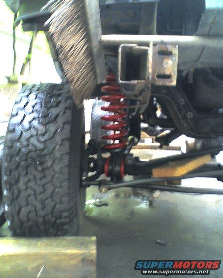 Truck chassis with a wire brush over a large tire and red coil spring