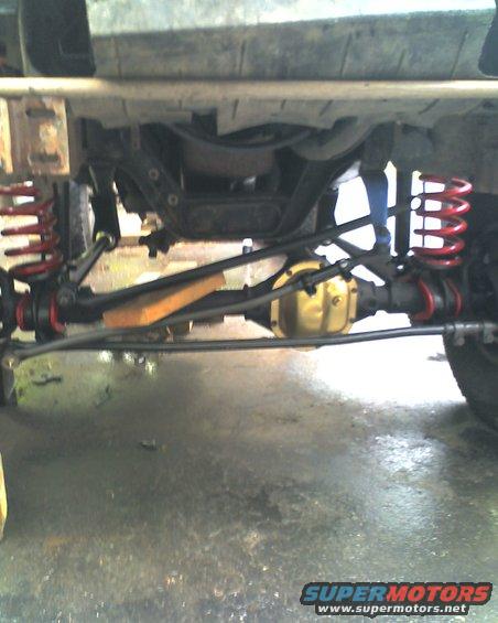 Underside view of a truck's suspension and drivetrain components, including red coil springs and a yellow differential