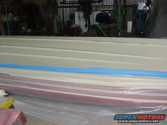 Boat hull with red and white stripes, covered in plastic sheeting, with blue tape on the upper section