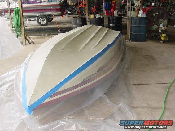 Boat hull covered in plastic sheeting and blue tape, resting on its side in a garage