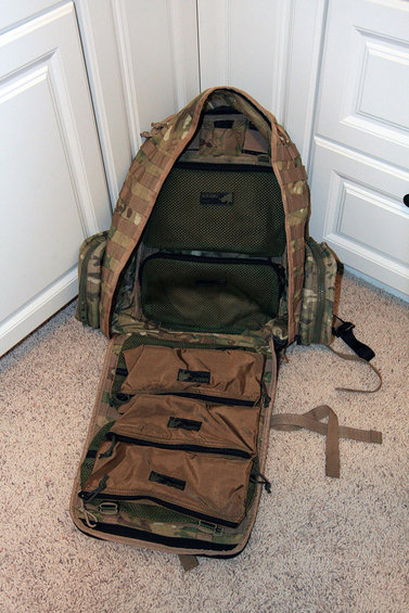 Open tactical backpack with multiple compartments and MOLLE webbing, shown on carpet