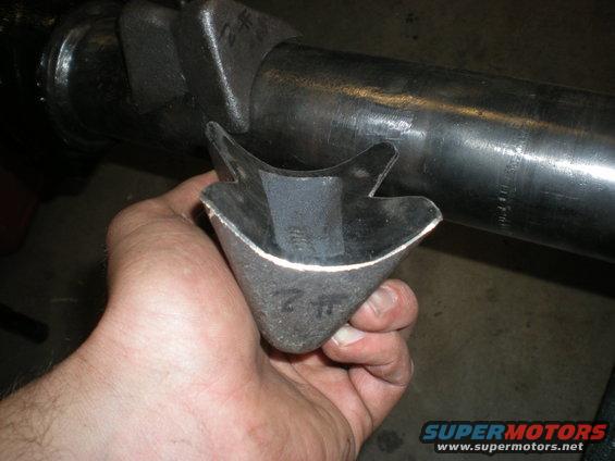 Hand holding a custom metal bracket part with a large metal tube in the background