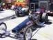 1973 Ford Mustang - A black dragster with "DON GARLITS Swamp Rat" lettering is parked next to another dragster, with trailers in the background.