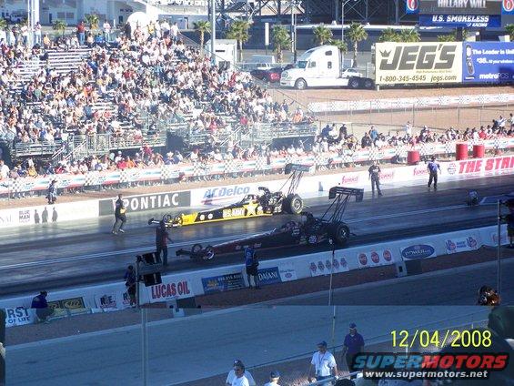 Two drag racing cars on a track with spectators in the stands