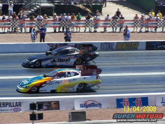 Two drag racing cars compete on a track, one black with 'Head Racing' and another colorful one with 'Levi, Ray & Shop, Inc.'