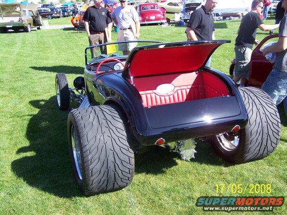 Black hot rod with red interior, large rear tires, open trunk, seen from rear