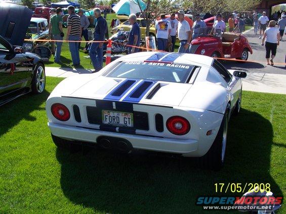White Ford GT with blue stripes on grass, license plate says FORD GT. Other cars and people in background