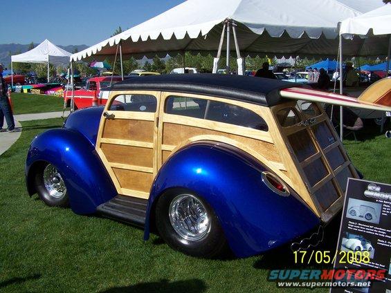 Blue and wood custom wagon with surfboard on roof, viewed from rear