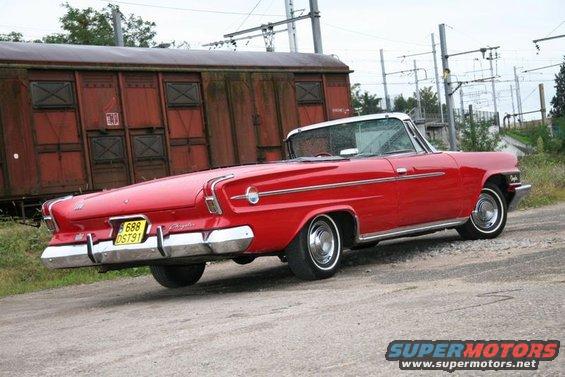 Red convertible with fins parked near a train car