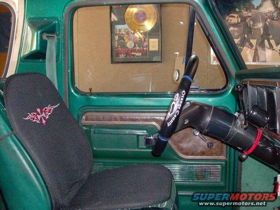 1978 Ford Bronco interior showing green door panel, seat cover with tribal design, and steering wheel with 'Orange County' text. Gold record on wall