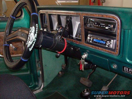 Green interior of a truck with wood trim dashboard, aftermarket radios, and a steering wheel cover that says "Orange County Choppers"