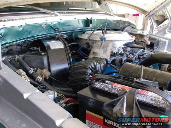 1978 Ford Bronco engine bay with green inner fenders, black air intake hose, and a Kirkland battery