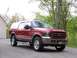 2005 Ford Excursion - A red 2005 Ford Excursion is parked on a paved surface, with a house and trees visible in the background.