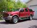 2005 Ford Excursion - This red 2005 Ford Excursion SUV is parked in front of a garage.