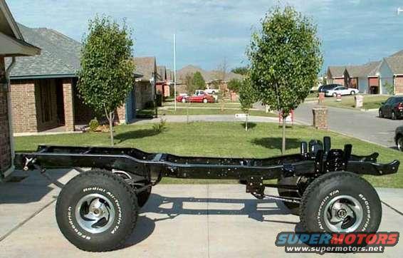 Bare black truck frame on jack stands with mounted wheels in a suburban driveway, houses behind