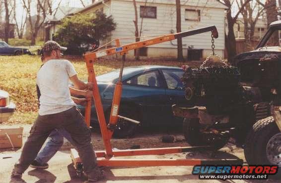 engine hoist lifting an engine, with a car in the background