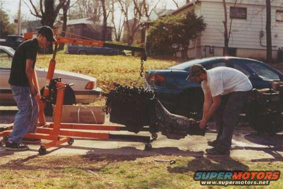 Engine being removed with an engine hoist, two cars visible