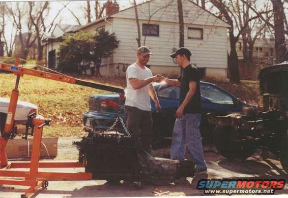 Engine being lifted by an orange engine hoist, two men shaking hands nearby