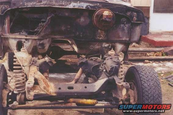 Front chassis of a heavily damaged vehicle, showing suspension and engine bay remnants. Appears to be a 4x4