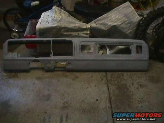 Gray dashboard assembly with multiple cutouts for gauges and controls