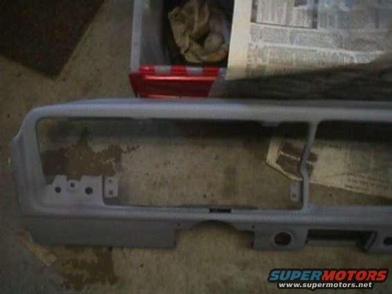 Gray dashboard frame with cutouts for gauges and radio, sitting on a concrete floor
