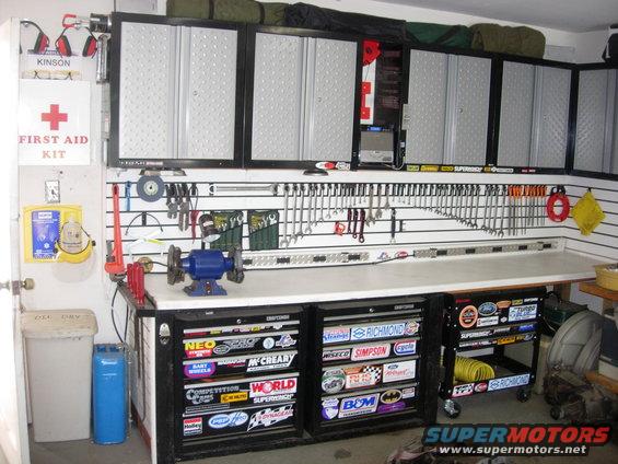 Garage workbench with tool cabinets, organized tools on wall, and many racing stickers on drawers